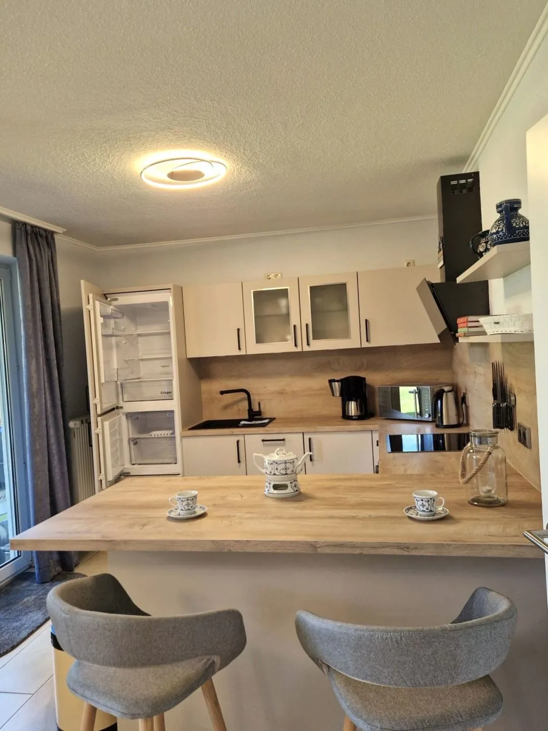 Küche mit Holztheke, zwei Barhockern und gedeckten Kaffeetassen