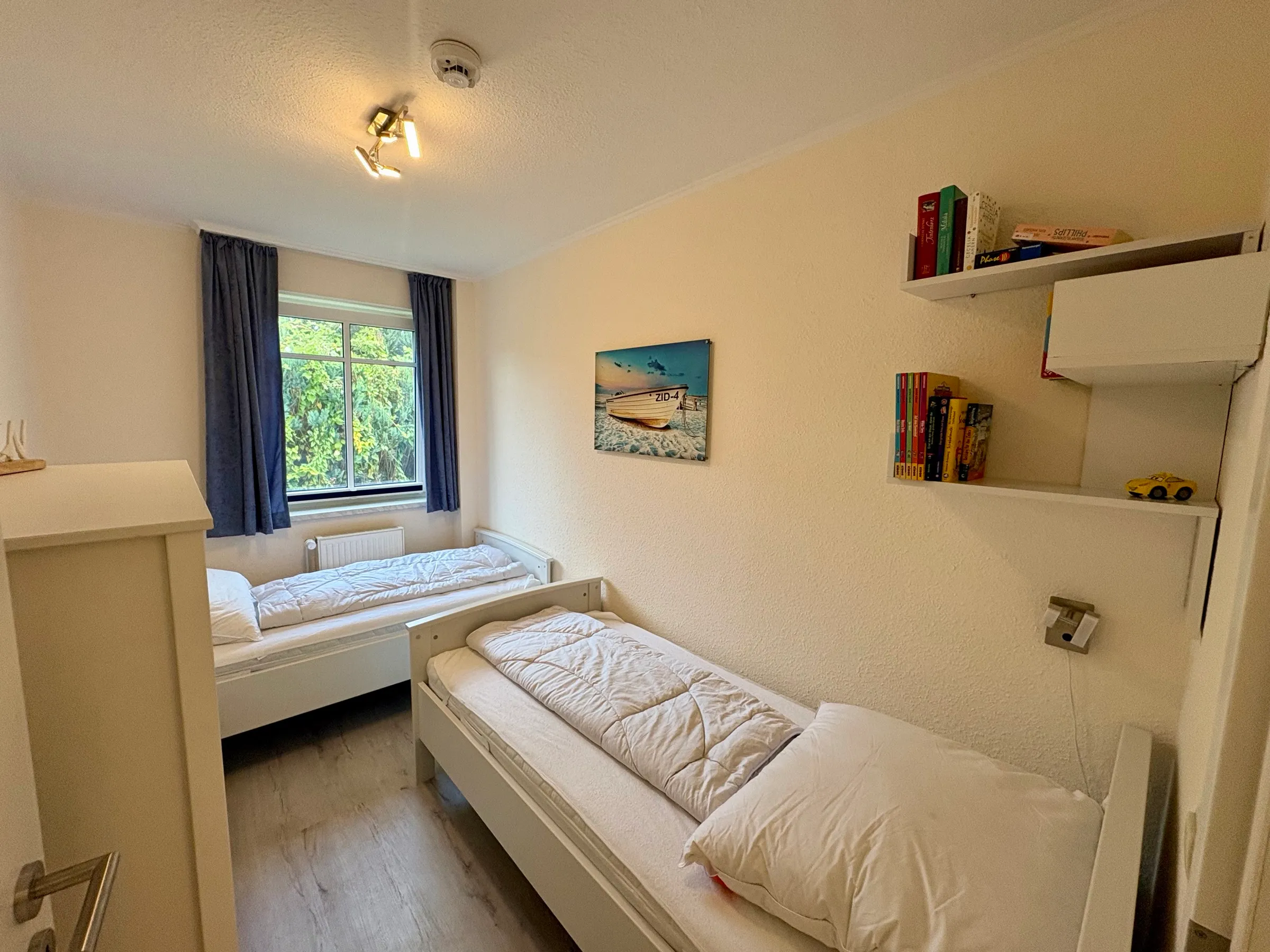 Zweites Schlafzimmer mit zwei Einzelbetten, Bücherregal und Fenster ins Grüne