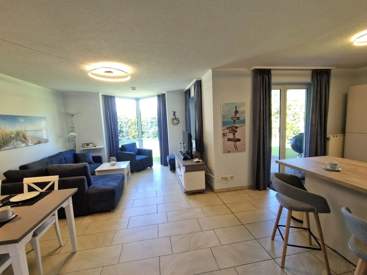 Offener Wohnbereich mit blauem Sofa, Essplatz und Küchentheke, große Fenster zum Garten
