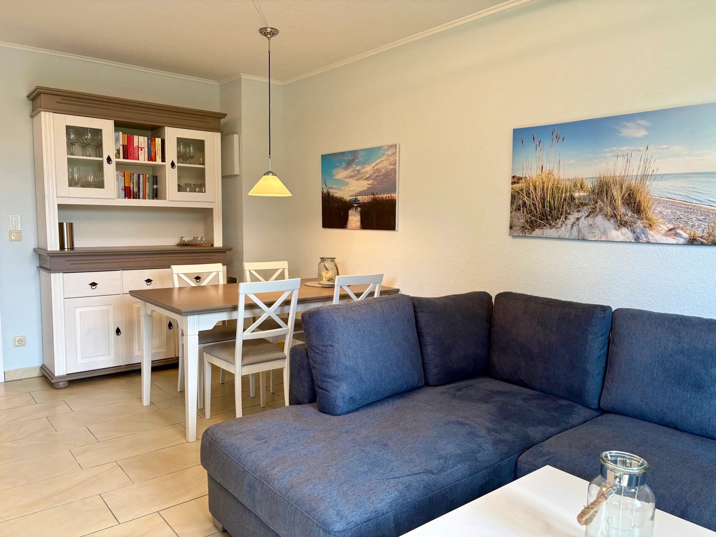 Heller Wohn- und Essbereich mit Sofaecke, Esstisch und Strandbildern